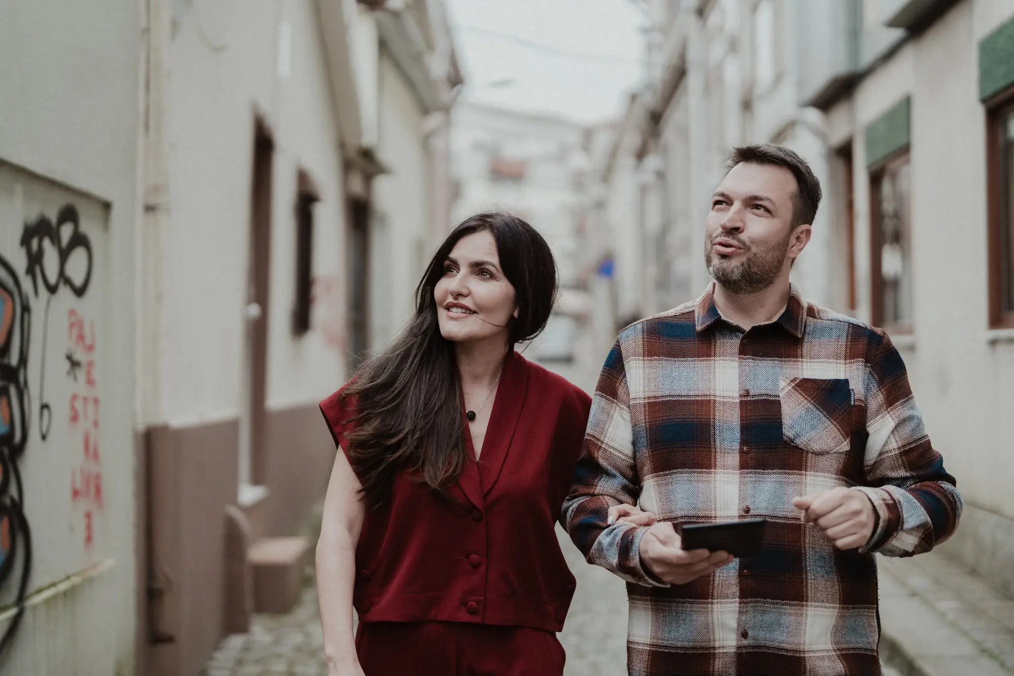 Two people walking down a narrow alleyway with graffiti on the walls.